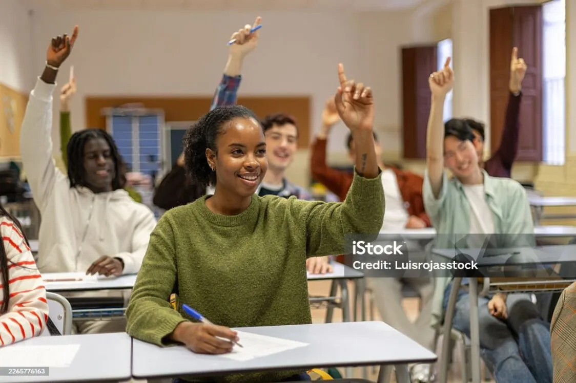 Student in a classroom with hands raised.